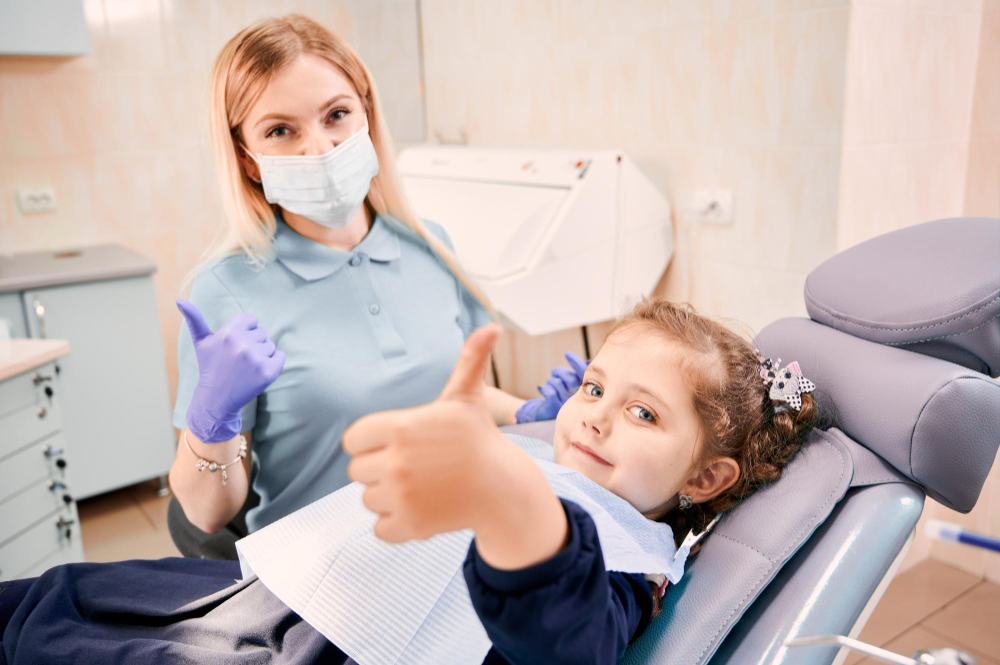 A young girl and a female dentist both giving "thumbs up" signs while the girl sits in the dental chair.