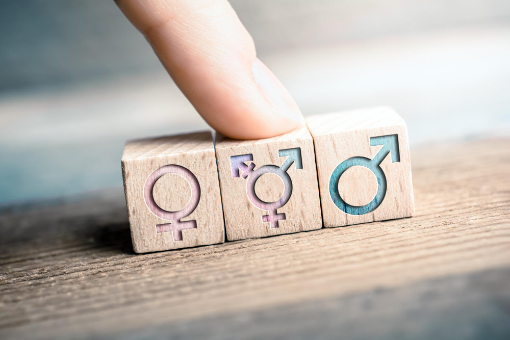 A colorful wooden symbol combining male, female, and transgender signs resting on a rainbow pride flag.