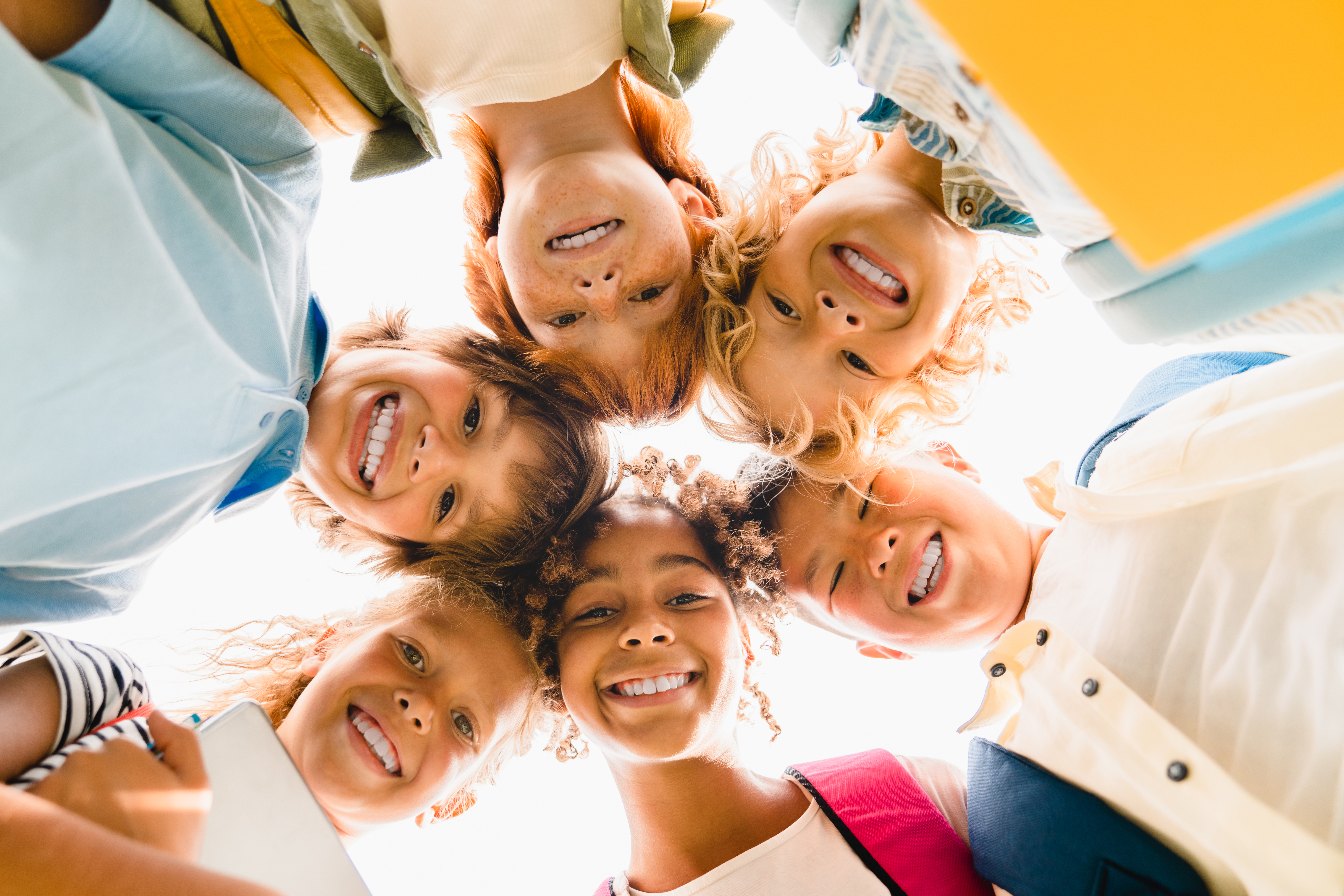 Diverse school kids looking down in a circle and smiling.